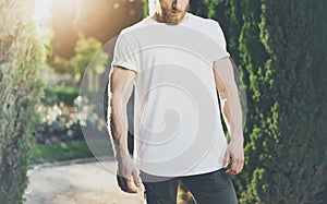 Photo Bearded Muscular Man Wearing White Blank t-shirt. Green Park Background and Sunlight effect. Horizontal Mockup