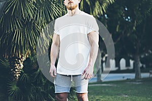 Photo Bearded Muscular Man Wearing White Blank t-shirt and shorts in summer time. Green City Garden Background,blurred