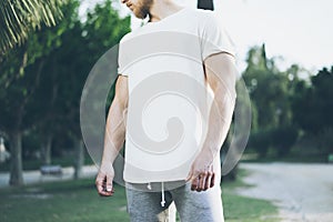 Photo Bearded Muscular Man Wearing White Blank t-shirt and shorts in summer time. Green City Garden Park Background