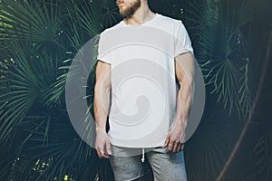 Photo Bearded Muscular Man Wearing White Blank t-shirt and shorts in summer time. Green Tree Palm Background. Horizontal