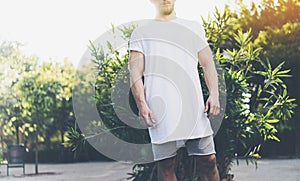 Photo Bearded Muscular Man Wearing White Blank t-shirt and shorts in summer time vacation. Green City Garden Park