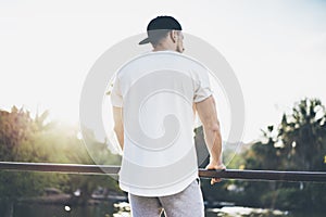 Photo Bearded Muscular Man Wearing White Blank t-shirt, snapback cap and shorts in summer time. Green City Garden Park