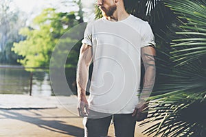Photo Bearded Muscular Man Wearing White Blank t-shirt in summer time. Green City Garden, lake and palms Background