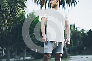 Photo Bearded Muscular Man Wearing White Blank t-shirt in summer time. Green City Garden.Relaxing time after hard work