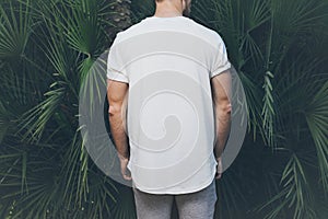 Photo Bearded Muscular Man Wearing White Blank t-shirt in summer time. Green huge palm Background. Back view. Horizontal