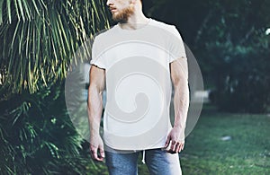 Photo Bearded Muscular Man Wearing White Empty t-shirt and shorts in summer vacations. Chilling time. Green City Garden