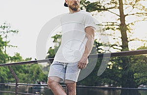 Photo Bearded Muscular Man Wearing White Empty t-shirt, snapback cap and shorts in summer vacation. Relaxing time near