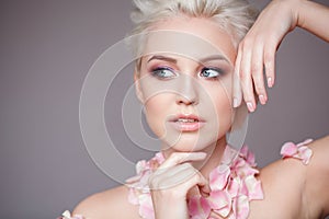 Photo of a beautiful blond woman with flower. Closeup attractive sensual face of white woman with curly hair. Smokey eye