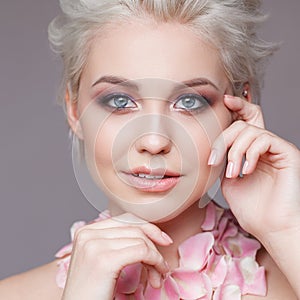 Photo of a beautiful blond woman with flower. Closeup attractive sensual face of white woman with curly hair. Smokey eye