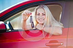 Photo of beautiful blonde woman with keys sitting in red car with open window