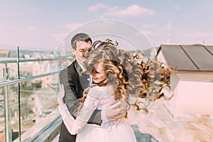 Photo of beautiful bride and groom dancing on roof top at sunny day