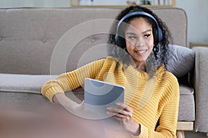 Photo of beautiful dark skin wavy lady homey mood holding digital tablet earflaps listening new audio sitting floor near couch