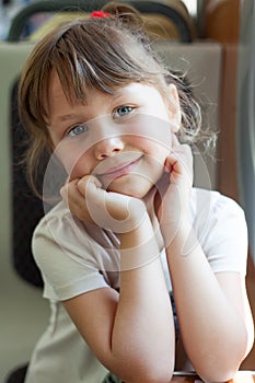 Photo of beautiful European cute girl traveling on train, holding hands near face. Close-up of a happy child looking at camera