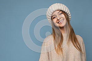 Photo of beautiful happy smiling young dark blonde woman isolated over blue background wall wearing beige warm sweater