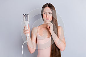 Photo of beautiful lady long hairstyle hold electric styler curler making straight curls wavy look side suspicious not