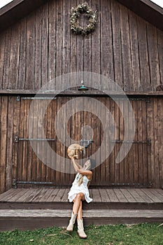 Photo of the beautiful and sexy blond woman in village, sitting on the stairs in front of wooden barn and playing with