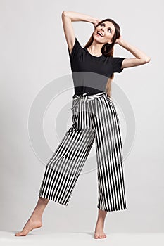 Photo of a beautiful slim woman in full growth, dressed in a black blouse and striped pants