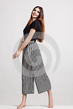 Photo of a beautiful slim woman in full growth, dressed in a black blouse and striped pants
