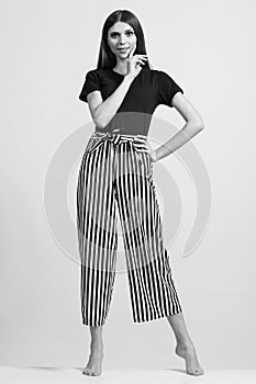 Photo of a beautiful slim woman in full growth, dressed in a black blouse and striped pants