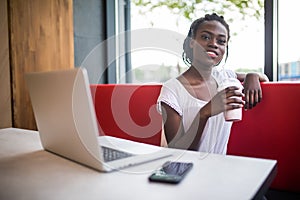 Photo of beautiful woman drinking milkshake sitting at cafe. Young african american woman sitting in a coffee shop and working on