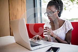 Photo of beautiful woman drinking milkshake sitting at cafe. Young african american woman sitting in a coffee shop and working on