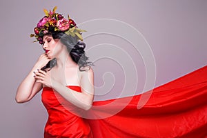 Beautiful young brunette woman model with bright flowers on her head in long red dress  on the purple background