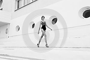 Photo of beautiful young girl with dark hair in elegant swimsuit, walking by the city street