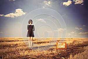 photo of beautiful young girl standing near suitcase in the field