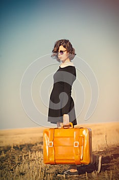photo of beautiful young girl standing with suitcase in the field