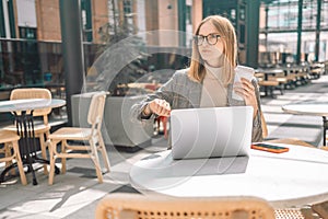 Photo of beautiful young pretty 30s woman sitting in cafe indoors using laptop computer and mobile phone looking at