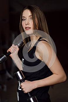 Photo of beautiful young woman with long hair and dumbbells at the gym