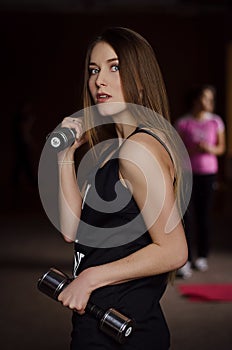 Photo of beautiful young woman with long hair and dumbbells at the gym