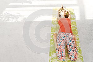 Photo of beautiful young woman lying on a yoga mat, resting after doing yoga exercises, lying in Savasana.