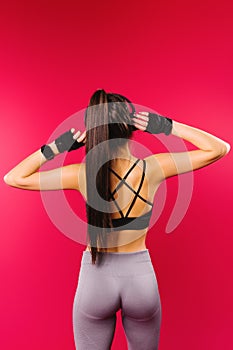 Photo from behind. A brunette with pumped up buttocks listens to music in large headphones on a red background. Sports