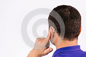 Photo from behind. An enlarged photo. Back of the head of a man pointing at the hearing aid in his ear. White background