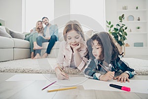 Photo of big family two children lying floor fluffy carpet making drawings while parents enjoy watching friendly adopted