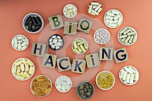 Photo on biohacking theme. wooden cubes with the inscription `biohacking`, and biologically active supplements,on coral background