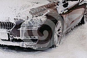 Photo of black car serviced at Sink. Dirty automobile covered with soap at carwash. Professional car wash. Vehicle cleaning photo