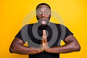 Photo of black man in t-shirt spectacles eyewear eyeglasses with hands folded in prayer and stupor on face begging to