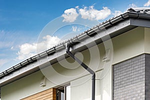 Photo of black rain gutter pipe on white wall under rood of new comfort house with element of wooden and brick facade and glass