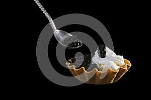 A photo of black sturgeon caviar in a tartlet and in the spoon isolated on the black background. Copyspace, place for text.