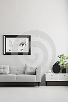 Photo in a black, thick frame on a gray wall, white sideboard and a gray sofa in a stylish living room interior with place for a P