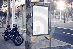 Photo blank lightbox on bus stop in the modern city. Authentic motobike parking close. Horizontal mockup, sunlight