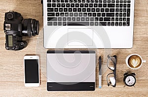 Photo blogger / photographer / it specialist`s typical office space table with laptop, blank screen, coffee cup and electronics.