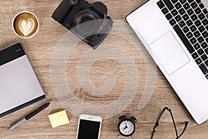 Photo blogger / photographer / it specialist`s typical office space table with laptop, blank screen, coffee cup and electronics.