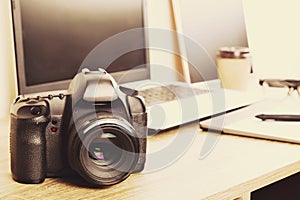 Photo blogger / photographer / it specialist`s typical office space table with laptop, blank screen, coffee cup and electronics.