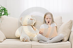 Photo of blond girl reading a book to her toy plush friend.