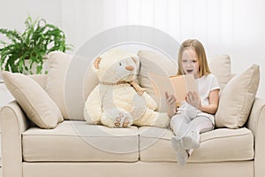 Photo of blond girl reading a book to her toy plush friend.