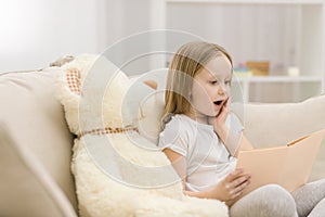 Photo of blond girl reading a book to her toy plush friend.