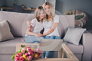 Photo of blonde peaceful mother and daughter look laptop hug woman day gift weekend rest indoors inside house home